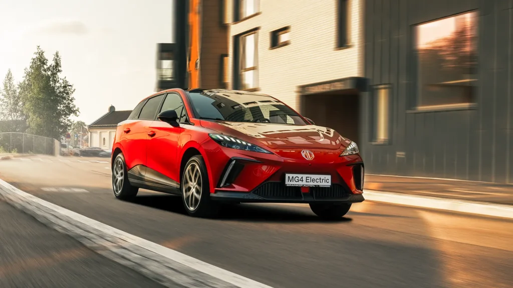 Rød MG4 elbil kjører i bygate med moderne bygninger.