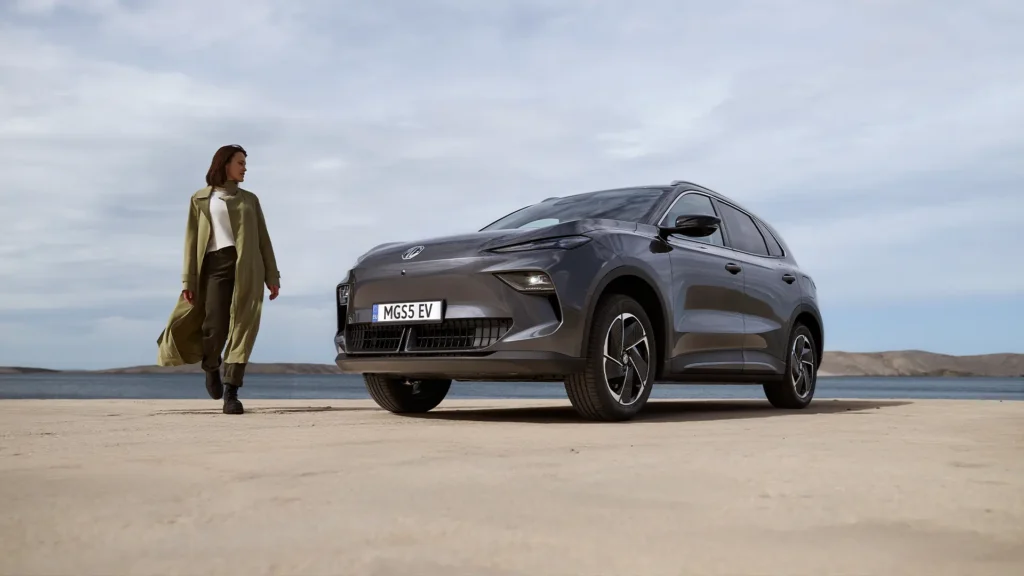 Kvinne nærmer seg grå MG SUV på sandete område.