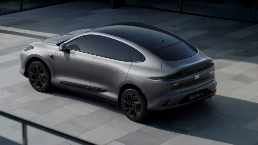 Sølvfarget elbil parkert ved en glassbygning.