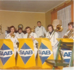 Lite band i hvite uniformer spiller messingblåsere bak SAAB-notestativer.