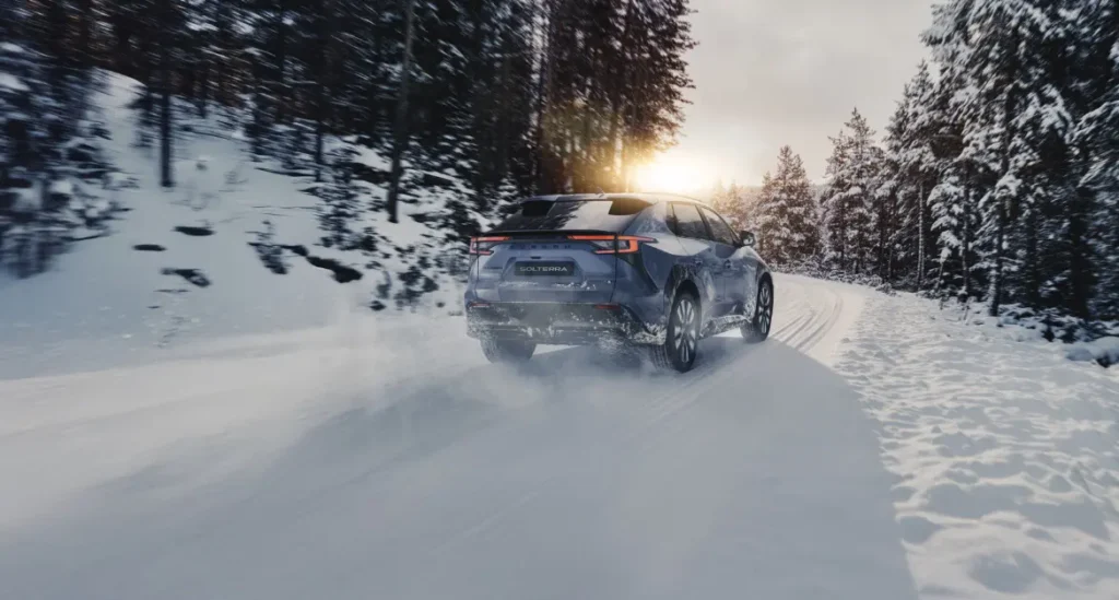 Subaru Solterra kjører på snødekt vei gjennom vinterlig skog.