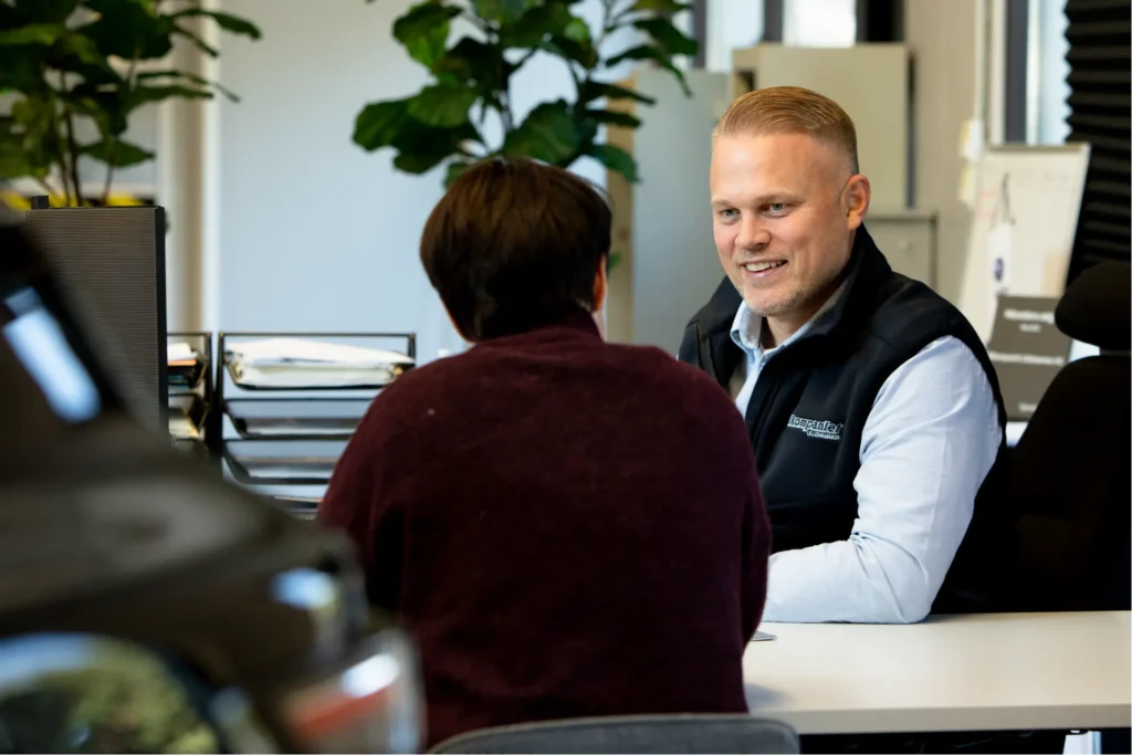 To personer diskuterer bruktbil ved et kontorbord.