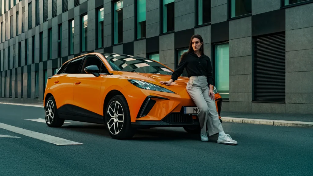 Kvinne lener seg mot oransje MG4 på en bygate.