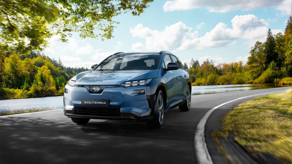 Blå elektrisk Subaru Solterra SUV kjører på vei ved en innsjø.