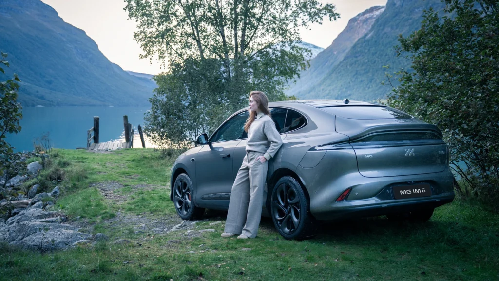 Person ved MG IM6 parkert på gress ved innsjø og fjell.