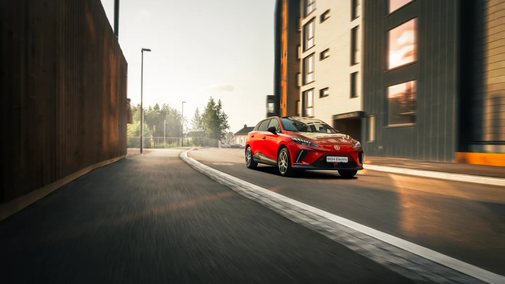 Rød MG IM6 kjører på tom bygate ved moderne leiligheter.