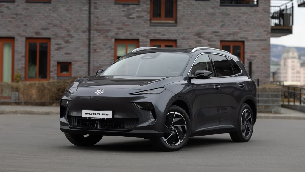 Mørk grå MG5 EV SUV parkert foran moderne murbygning.