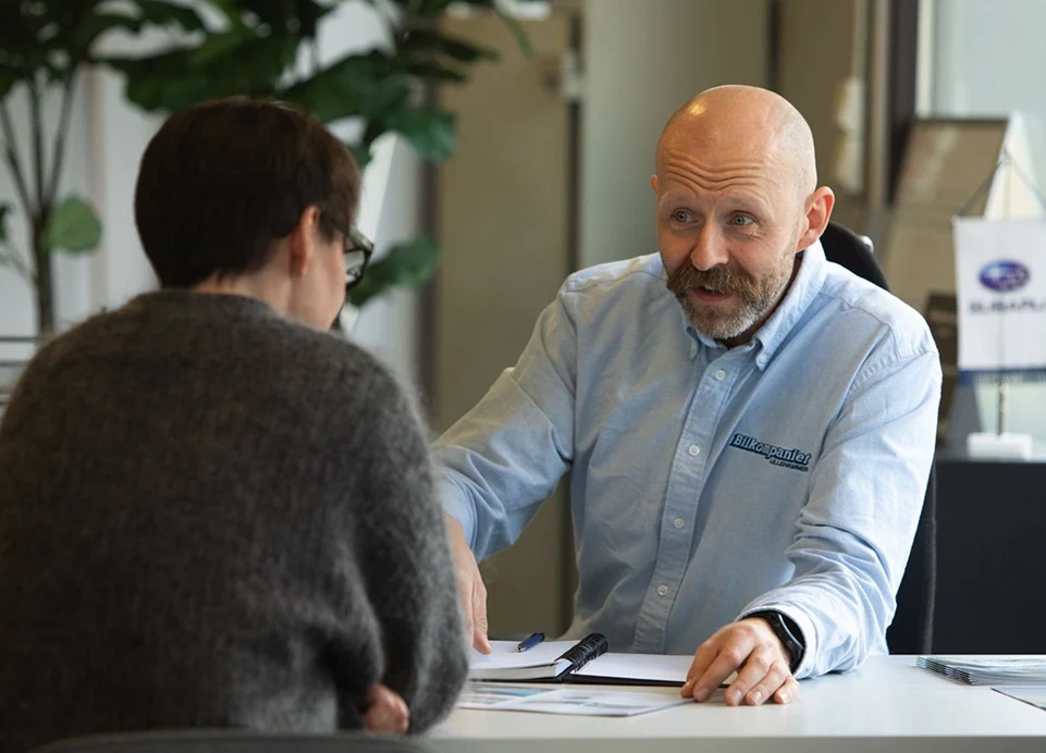 To personer diskuterer bruktbilpapirer ved et kontorbord.